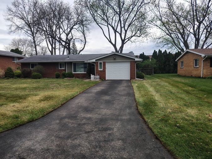 A brick ranch house with a white garage door, an asphalt driveway and a freshly mown lawn with mowing lines, under bare trees.