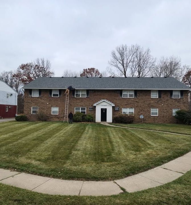 A brick apartment building with a striped, freshly mown lawn in front and a concrete walk curving along the bottom of the frame.